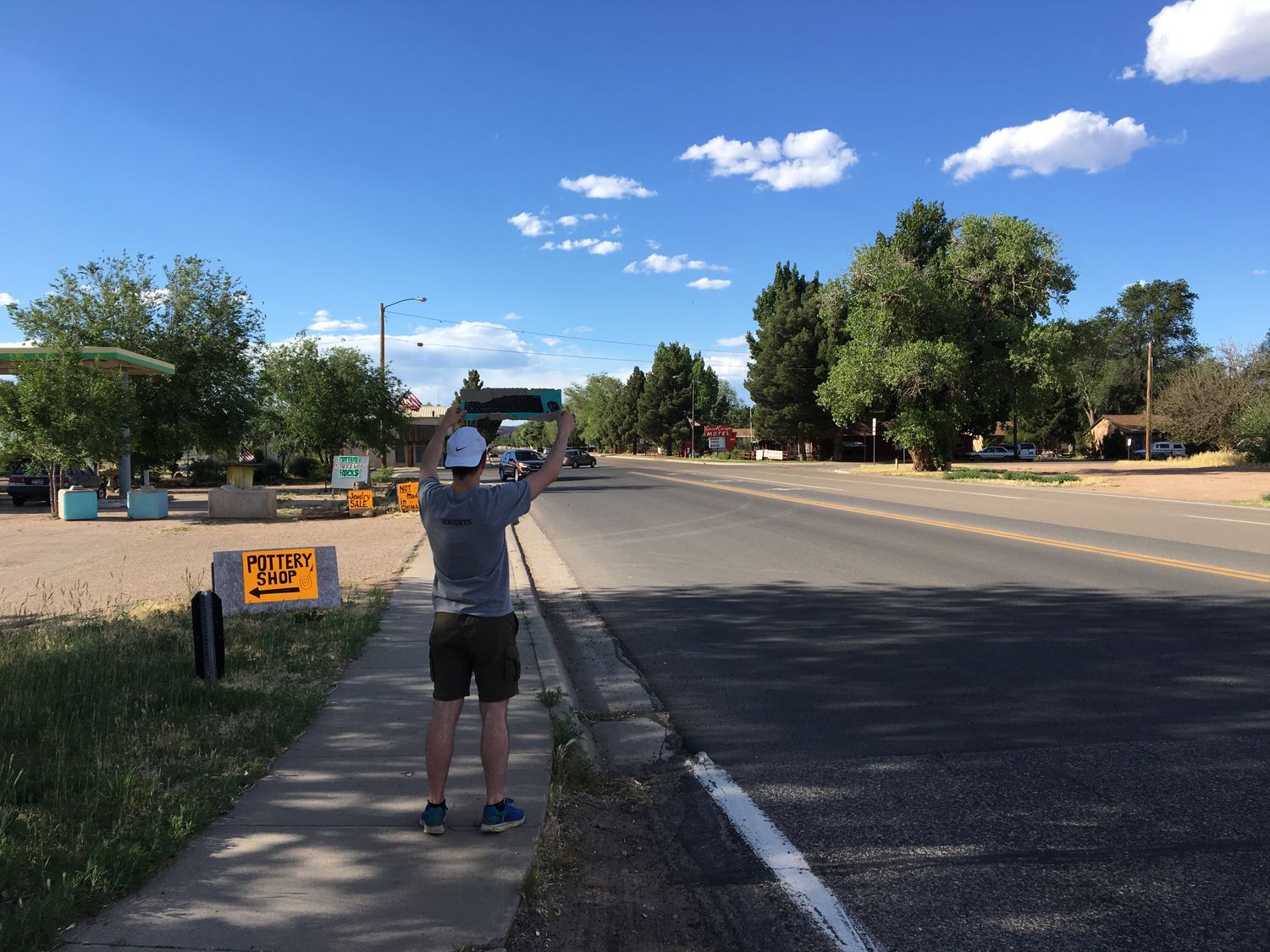 Man holding a sign while hitchhiking along a small-town Arizona road